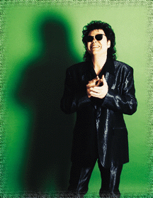 Photo of Ronnie wearing all black against green background smiling and clapping hands.